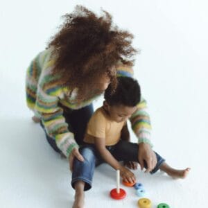 An adult and child play with colorful toys on a white background, showcasing joy and creativity.