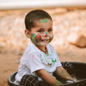 Happy child with colorful face paint playing in a basin outdoors, smiling with joyful expression.